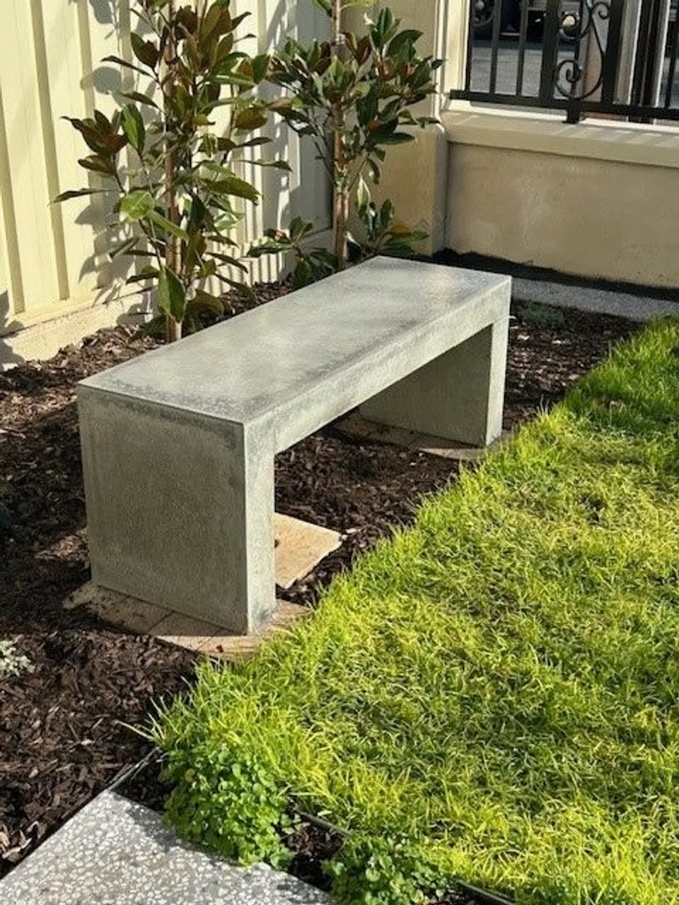 Banco maciço de concreto em um jardim, ao lado de plantas